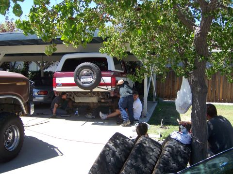 1991 Ford Bronco - Several individuals work on the undercarriage of a 1991 Ford Bronco parked in a driveway.