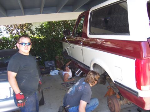 1991 Ford Bronco - Mechanics work on a two-tone red and white Ford Bronco, likely installing a lift kit.