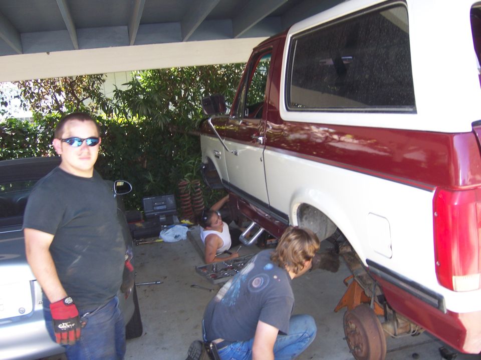 Two-tone red and white Ford Bronco with lift kit components visible