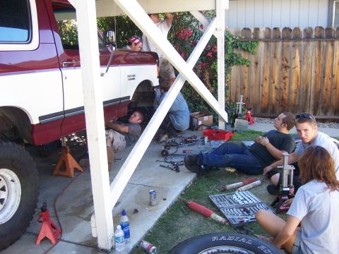 1991 Ford Bronco - Several people are working on a lifted 1991 Ford Bronco in a driveway, with tools and parts laid out.