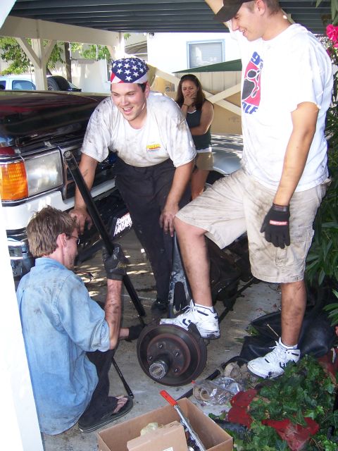 1991 Ford Bronco - Three men are gathered around the front suspension of a vehicle, appearing to be in the process of installing a lift kit.