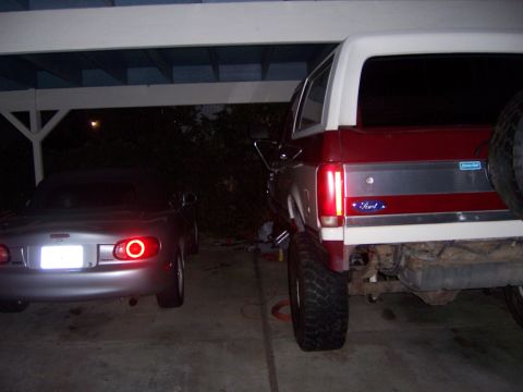 1991 Ford Bronco - Two vehicles parked under a covered area, one a lifted Ford Bronco and the other a Mazda Miata.