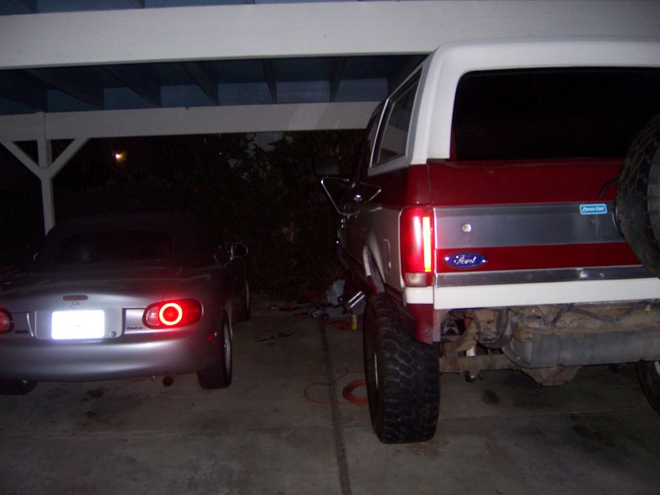 Rear view of a lifted Ford Bronco next to a Mazda Miata