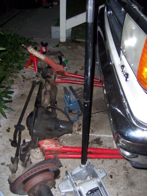 1991 Ford Bronco - Vehicle parts, including an axle and brake rotor, are laid out on the ground next to a white vehicle.