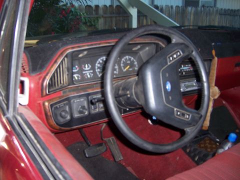 1991 Ford Bronco - Interior view of a red vehicle's dashboard and steering wheel, showing analog gauges and wood trim details.