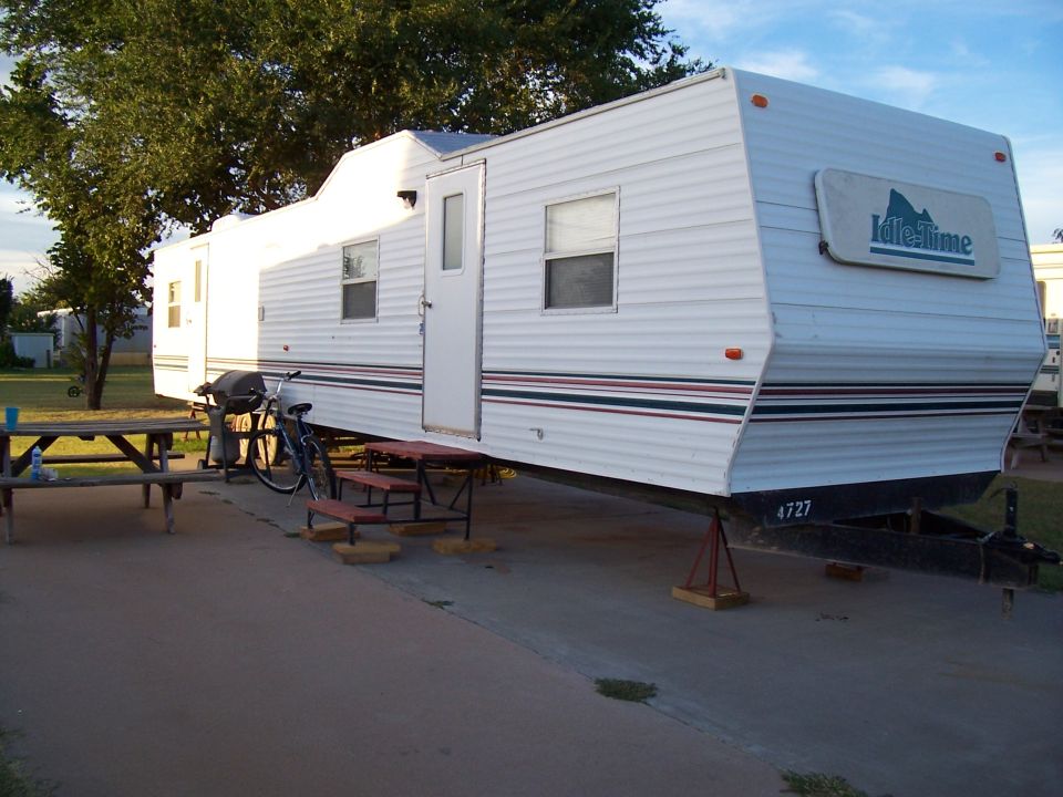 Camper trailer with 'Idle-Time' logo parked on a paved surface next to a picnic table and bicycle