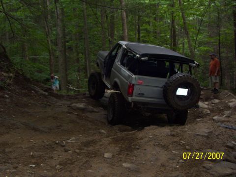 1978 Ford Bronco - A gray Ford Bronco navigates a challenging off-road trail in a wooded area.