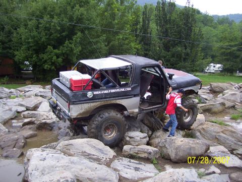 1978 Ford Bronco - A modified 1978 Ford Bronco tackles a rocky obstacle course, with a young person exiting the driver's side.