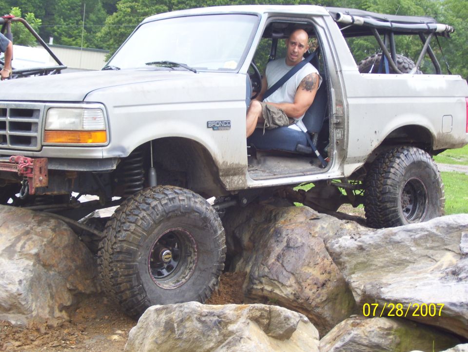 Man in driver's seat of lifted Bronco on rocks. Bronco badge visible on fender