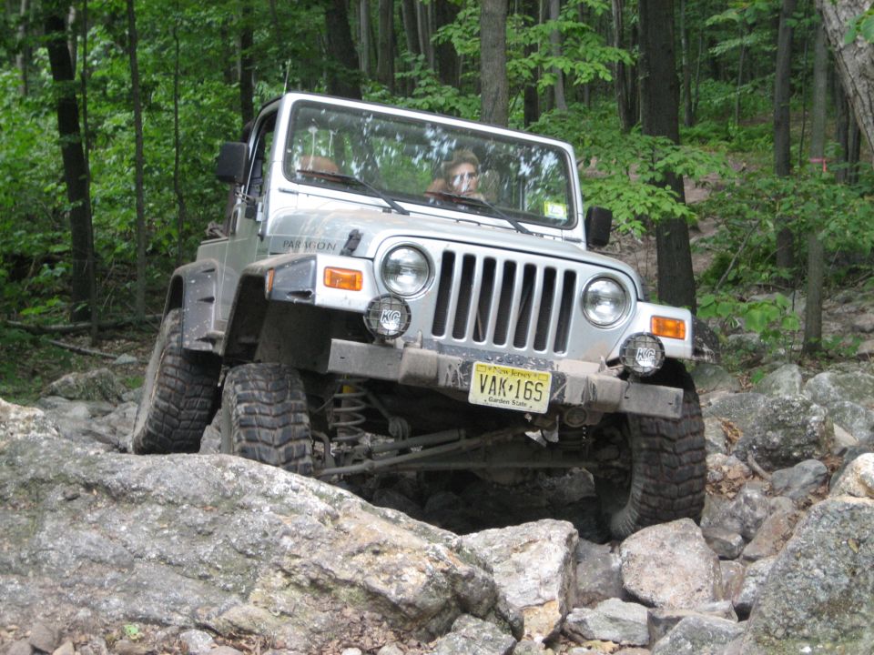 Silver Jeep Wrangler driving over rocks, front view. License plate VAK-16S