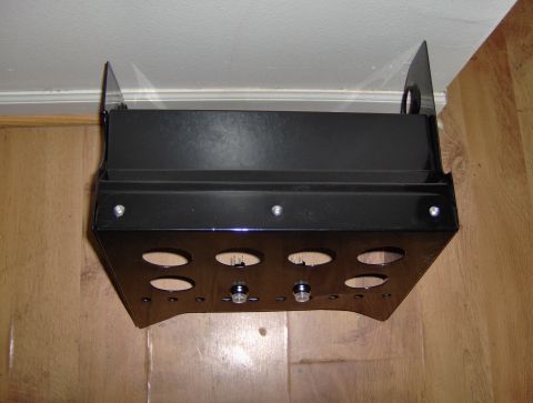 1978 Ford Bronco - A black metal console part, possibly for a vehicle, is shown mounted against a wall and wooden floor.