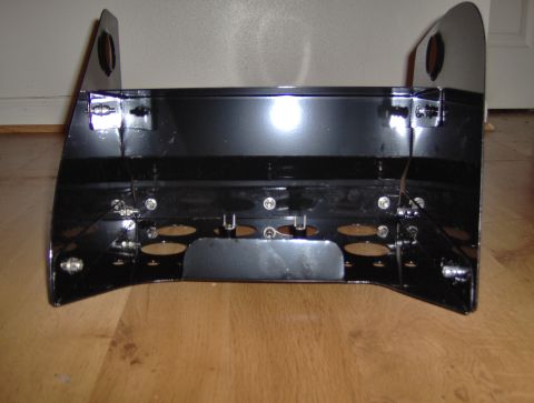 1978 Ford Bronco - A black painted metal console part is shown from the front, resting on a wooden floor.