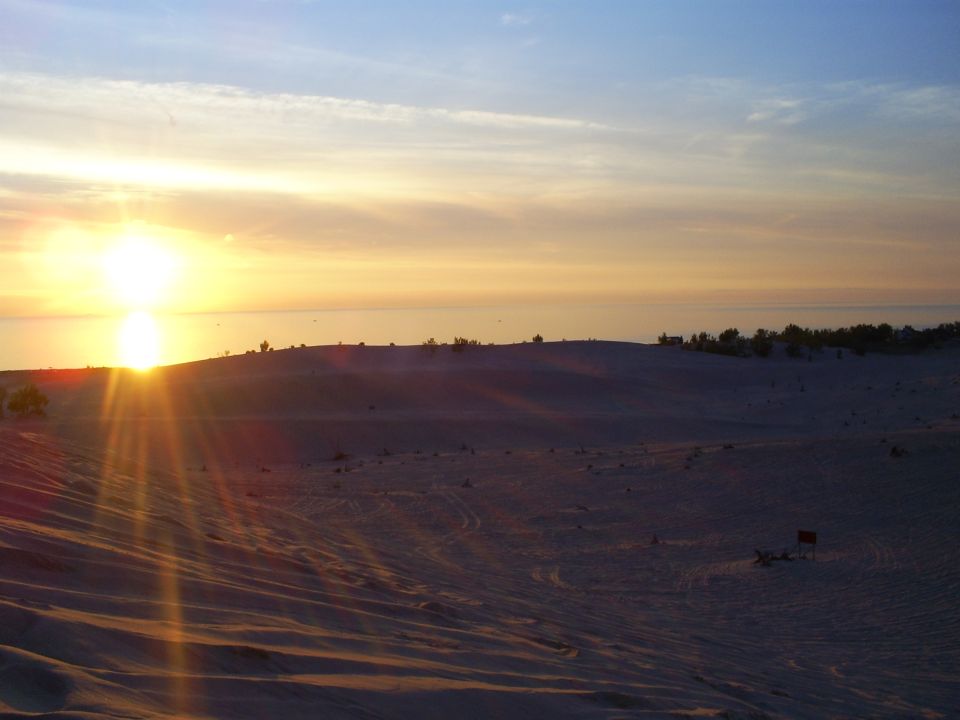 dunes and ocean at sunset with sun low on the horizon