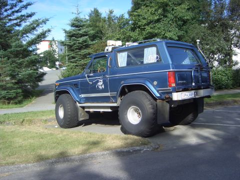 1974 Ford Bronco - This blue SUV is equipped with extremely large tires and a roof rack, suggesting off-road capabilities.