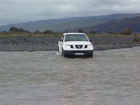 1974 Ford Bronco - A white Nissan pickup truck navigates a rocky riverbed under an overcast sky.