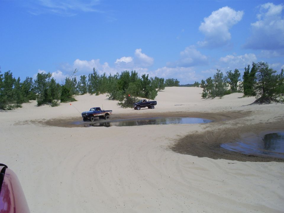 Two trucks driving through sand dunes with puddles of water