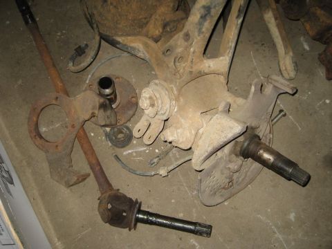 1995 Ford Bronco - Various corroded automotive parts, including a spindle and drive shaft, are laid out on a floor.