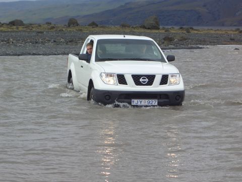 1974 Ford Bronco - A white Nissan pickup truck navigates through a shallow river, with two occupants visible inside.