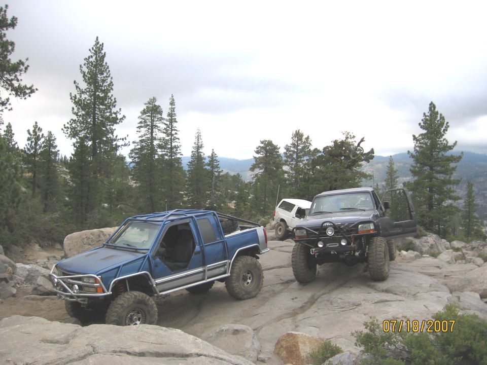 Caged blue pickup, dark blue Ford SUV with winch bumper and white Bronco parked on granite slabs
