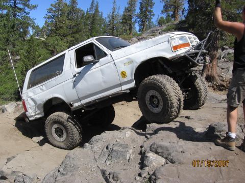 1994 Ford Bronco - Modified white Ford Bronco tackles a challenging rocky trail on a sunny day.