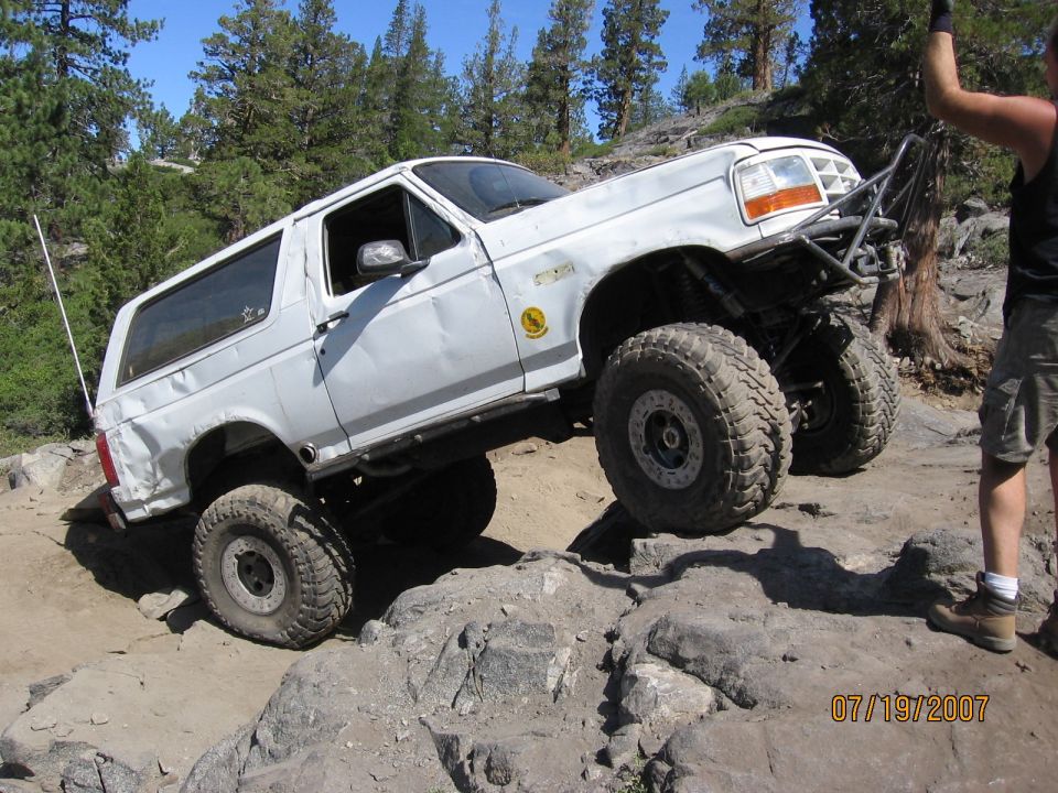 White lifted Ford Bronco flexing suspension over granite rocks on trail