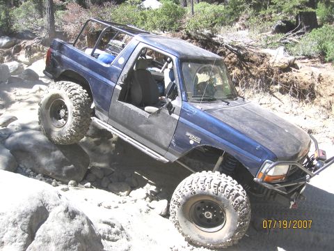 1994 Ford Bronco - A blue 1994 Ford Bronco is shown tackling a challenging rocky trail with its doors removed.