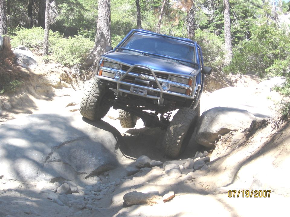 Lifted blue Chevrolet SUV with roll cage and winch bumper crawling a granite rock notch