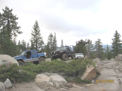 1994 Ford Bronco - Multiple off-road vehicles navigate a rocky trail surrounded by trees.