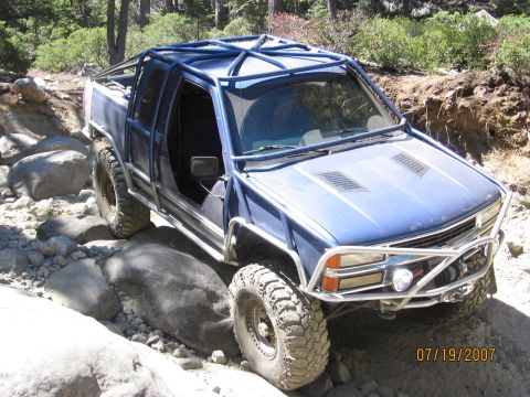 1994 Ford Bronco - Modified pickup truck with extensive roll cage and off-road tires on a rocky trail.