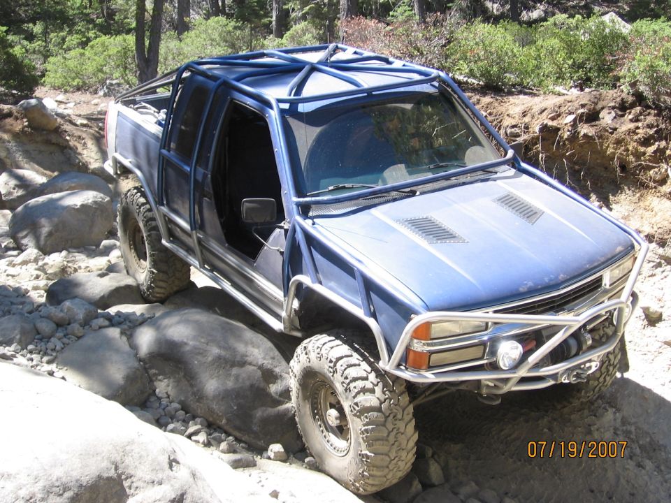 Blue 4x4 with exterior roll cage and winch bumper crawling over boulders on rock trail