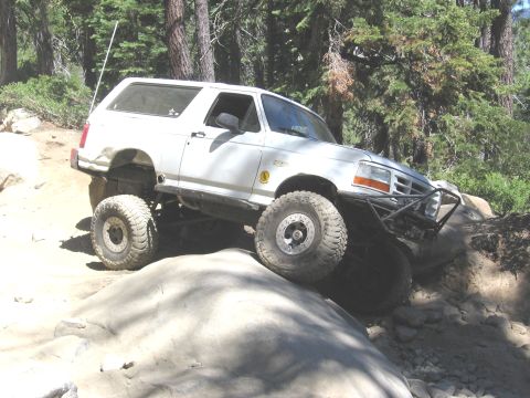 1994 Ford Bronco - White Ford Bronco navigates a rocky trail with large off-road tires.