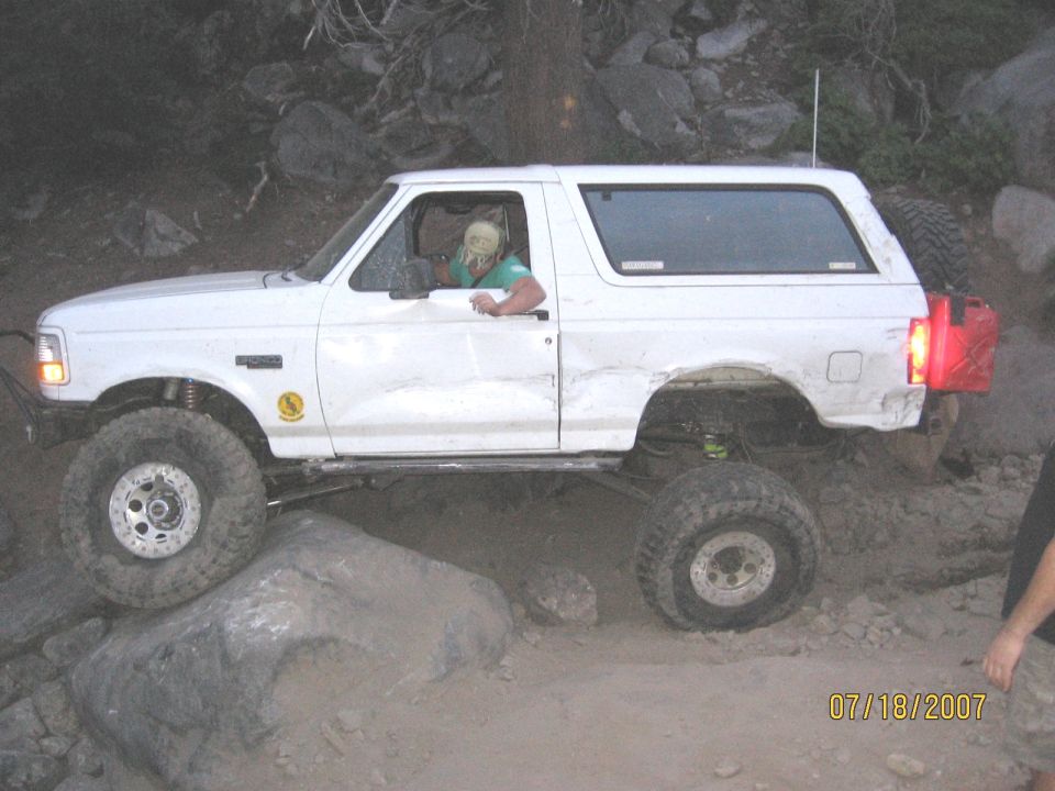 Lifted white two-door SUV on mud-terrain tires crawling over boulders on a rocky trail