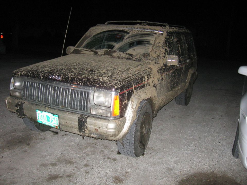 Mud-covered 1993 Jeep Cherokee, 3/4 front view. License plate visible