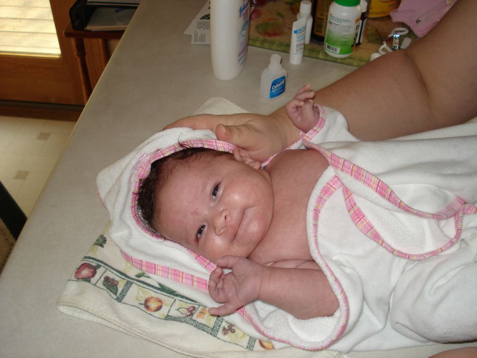 Baby wrapped in a white towel with pink trim, lying on a patterned towel