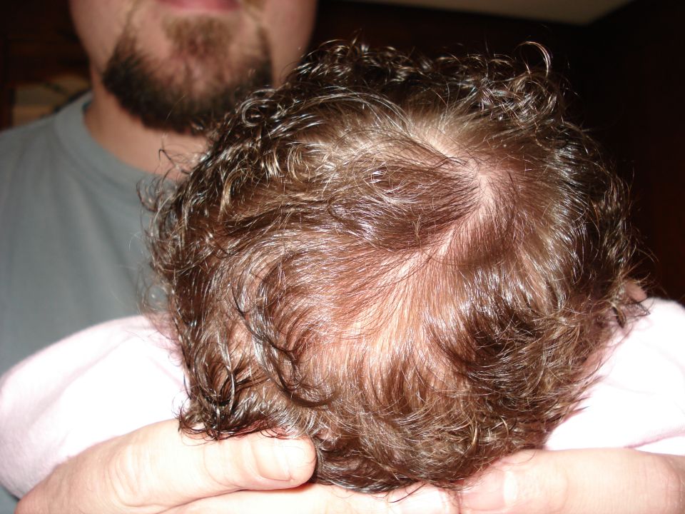 Person holding a baby's head with curly brown hair