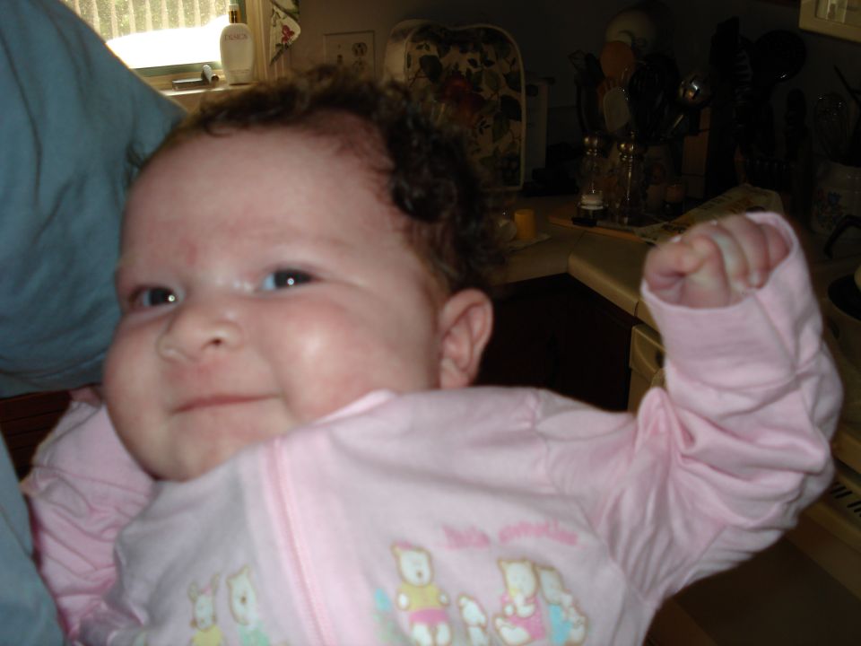 Baby in pink pajamas with cartoon animals, flexing arm