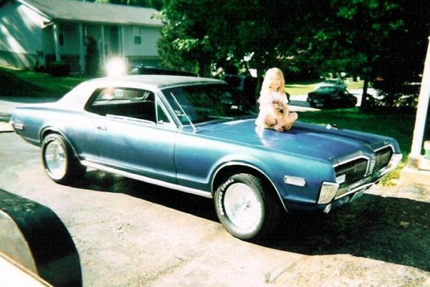 Blue coupe with a child sitting on the hood. The car has a vinyl top and chrome trim