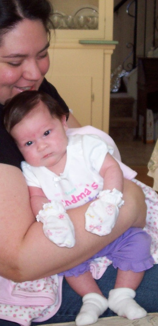Woman holding a baby wearing a white onesie with 'Grandma's' text and white mittens