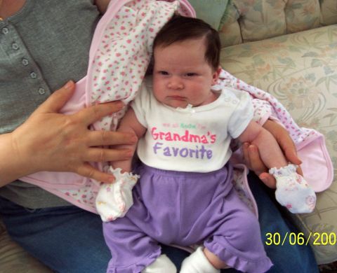 2000 Ford Crown Victoria - A baby is held by someone, wearing a shirt that says "Grandma's Favorite" and purple pants.