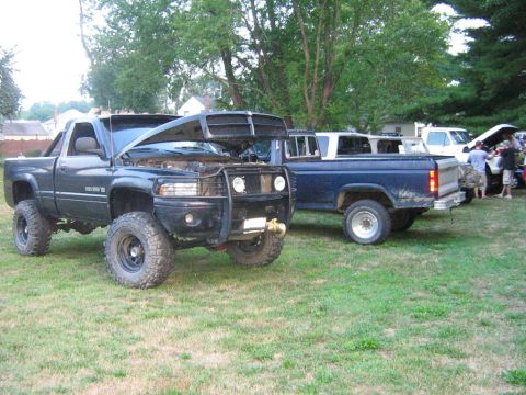 1990 Ford Bronco - Two modified pickup trucks are parked on a grassy lawn, with one having its hood open.
