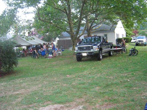 1990 Ford Bronco - A dark blue Ford F-Series pickup truck is parked on a lawn with people gathered under a tent in the background.