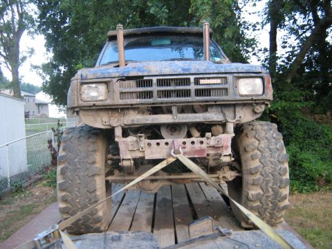 1990 Ford Bronco - A heavily modified blue Toyota pickup truck is shown from the front, secured to a trailer with large off-road tires and prominent exhaust p…