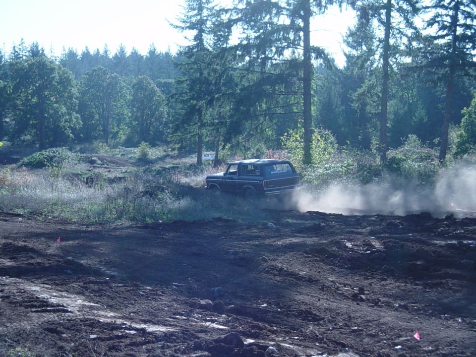 Dark Ford pickup sliding through a dusty dirt field ringed by evergreens