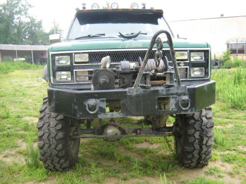 1990 Ford Bronco - This heavily modified green truck features a prominent winch and bull bar on its front end.
