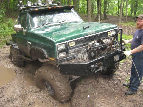1990 Ford Bronco - Off-road pickup truck with winch is stuck in a muddy forest trail.