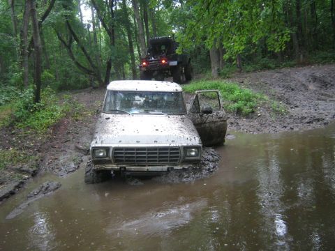 1990 Ford Bronco - A white Ford Bronco navigates a muddy trail, with another vehicle following in the background.