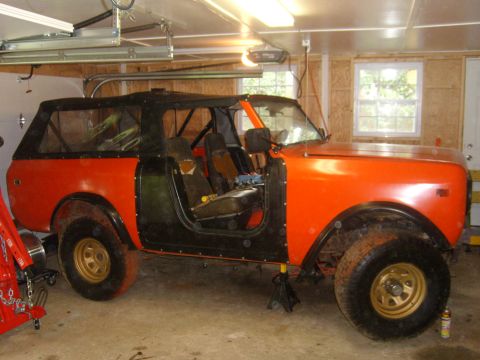 1994 Ford Bronco - Orange off-road vehicle with black soft top and doors removed, jack stands supporting the front.
