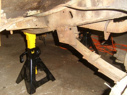 1994 Ford Bronco - Undercarriage view of a vehicle supported by jack stands, showing rusted frame and suspension components.