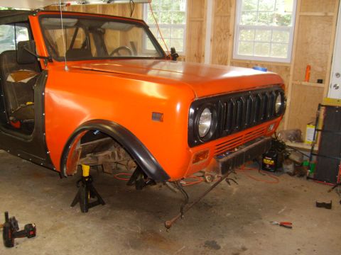 1994 Ford Bronco - This orange International Harvester Scout II is undergoing repairs in a workshop, with its front end elevated on jack stands.