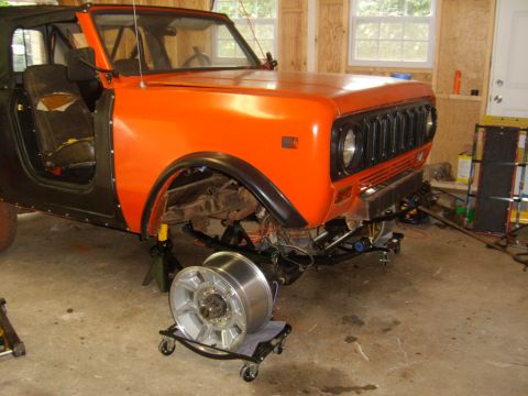 1994 Ford Bronco - An orange International Harvester Scout II is undergoing repairs in a garage, with its front wheel removed.